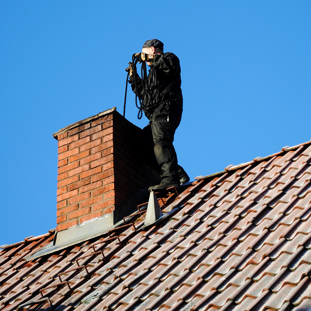 Chimney professional inspecting and cleaning a residential chimney from the roof