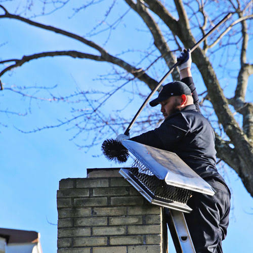 Chimney sweep servicing a metal chimney cap from a ladder