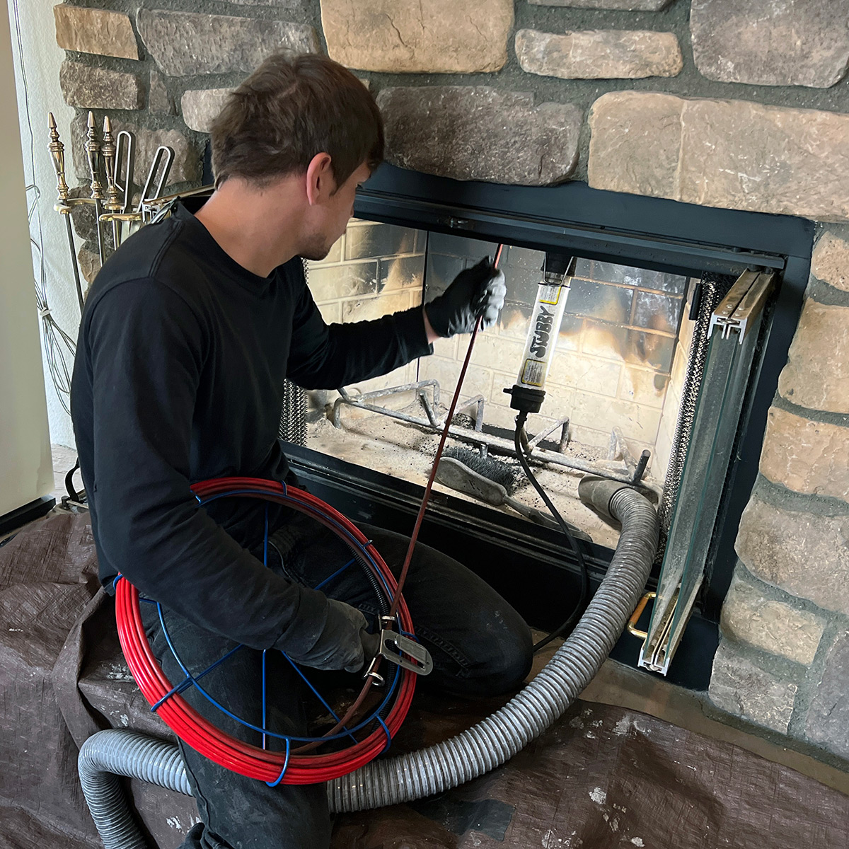 Chimney technician cleaning a glass-front fireplace with professional equipment